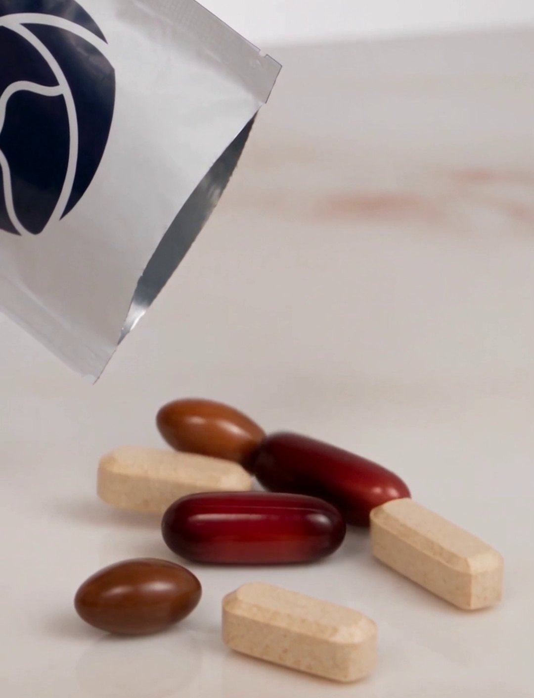 One sachet tipped open with its seven pieces on a counter: three tablets and four softgels